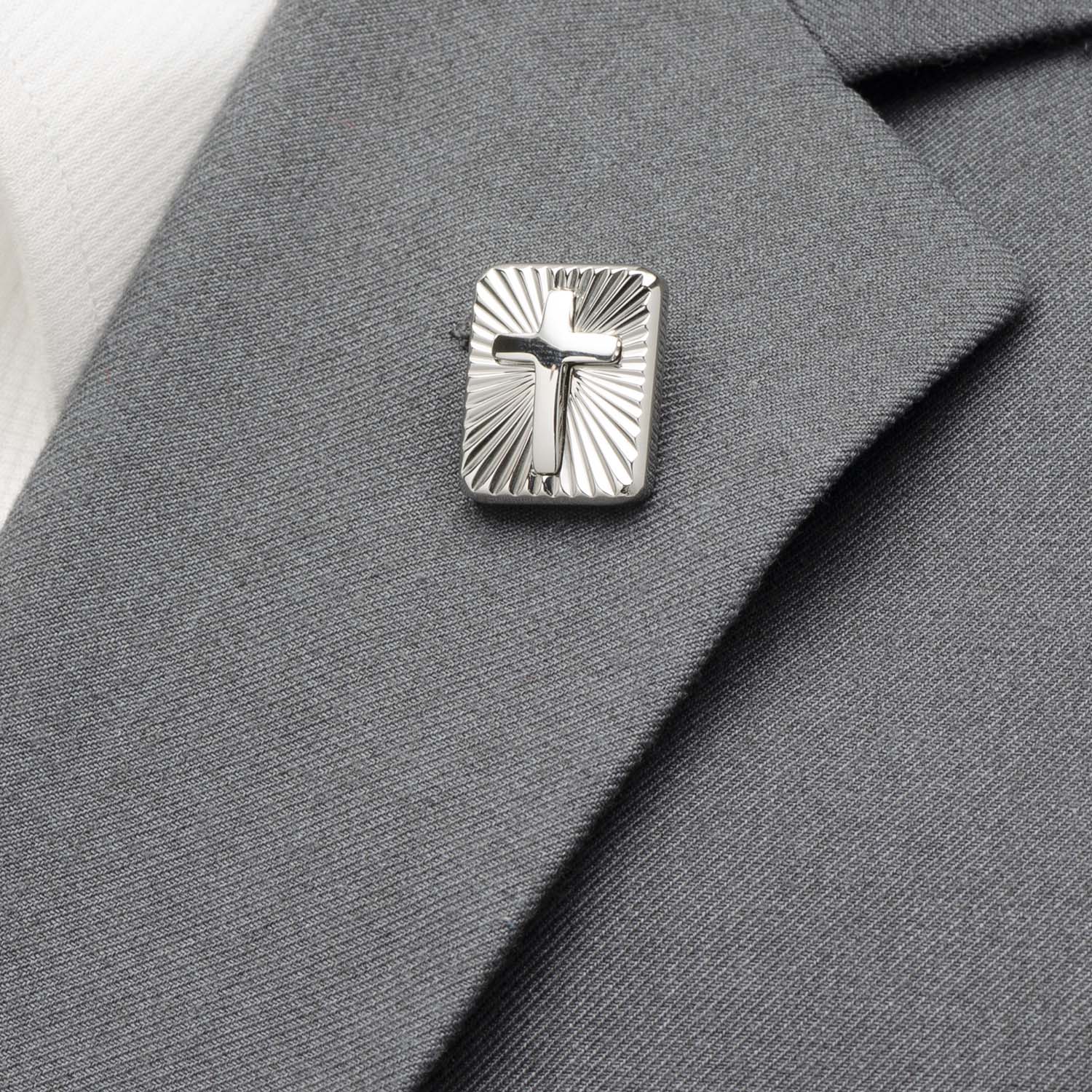 Silver cross lapel pin on a gray suit jacket