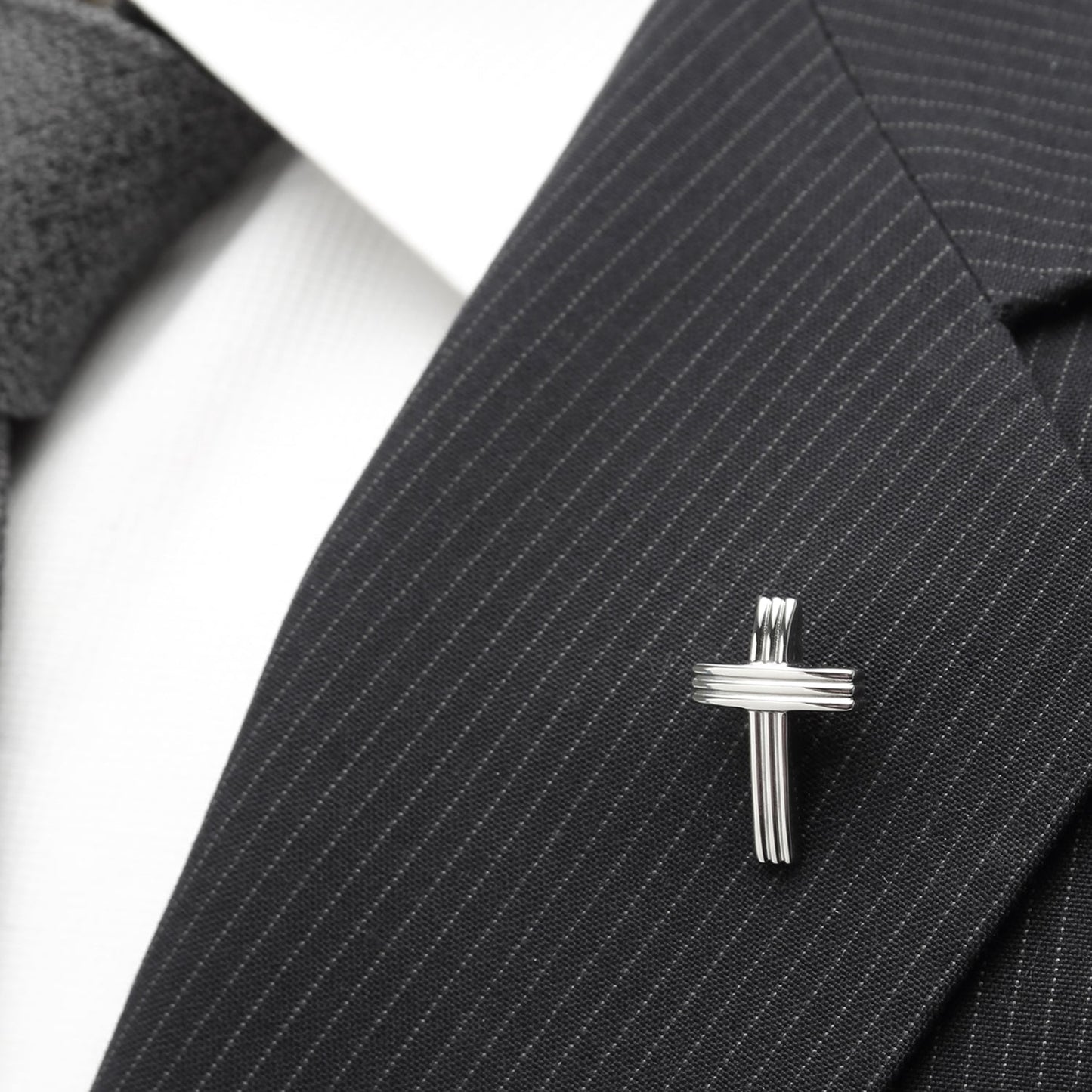 Silver cross lapel pin on a black pinstripe suit jacket
