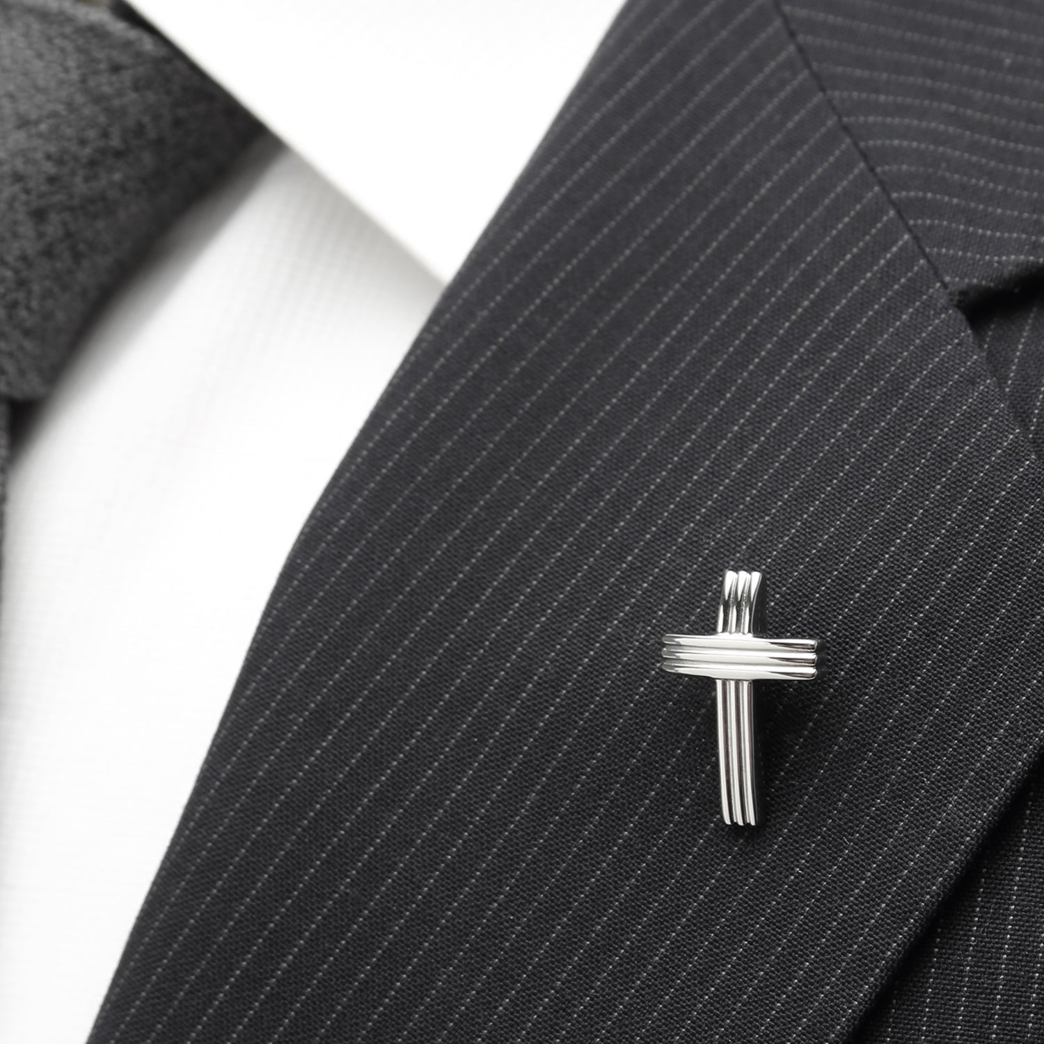 Silver cross lapel pin on a black pinstripe suit jacket