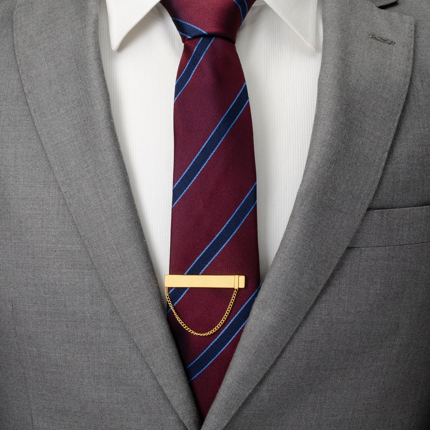 Maroon tie with blue stripes and a gold tie clip on a gray suit jacket.