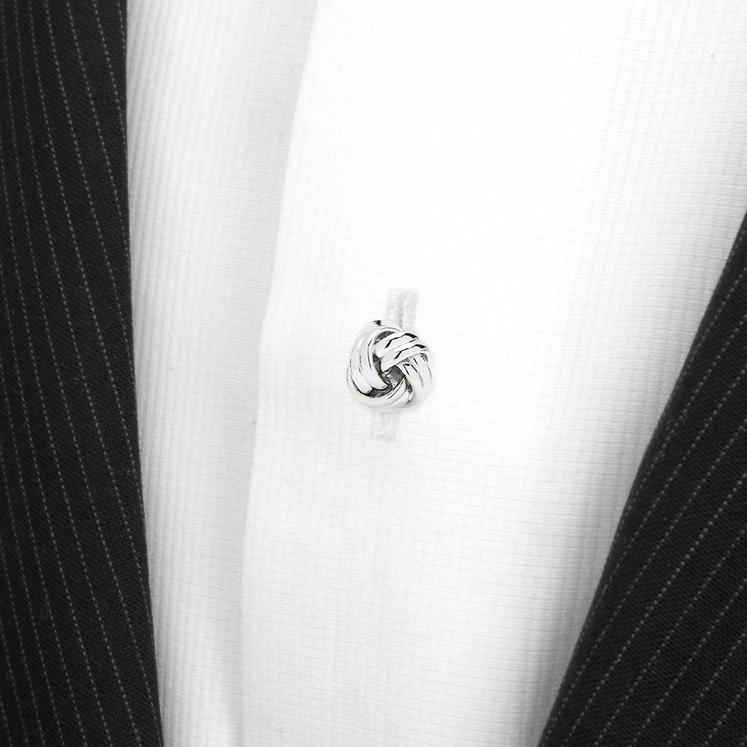 Close-up of a silver knot earring on a black and white striped fabric background