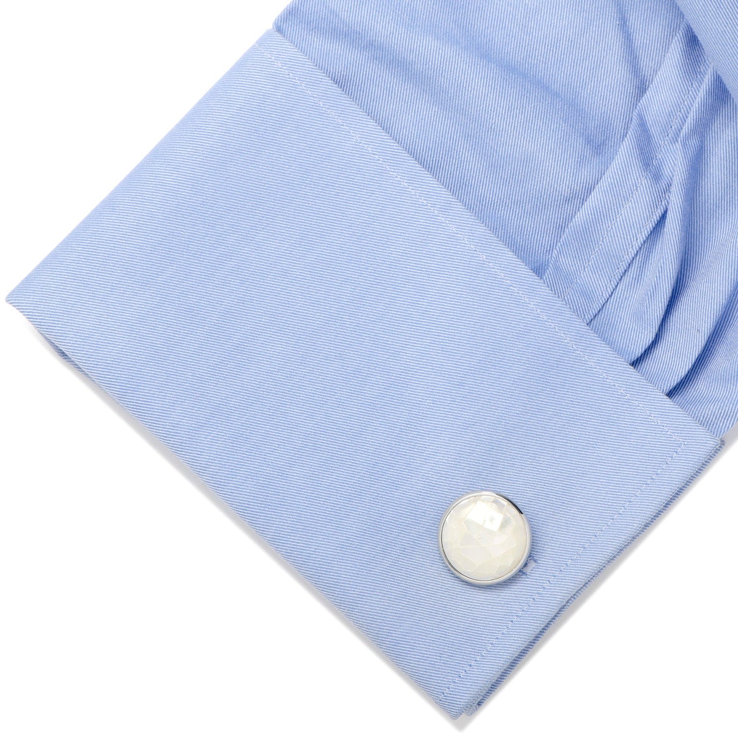Close-up of a light blue shirt cuff with a pearl button on a white background