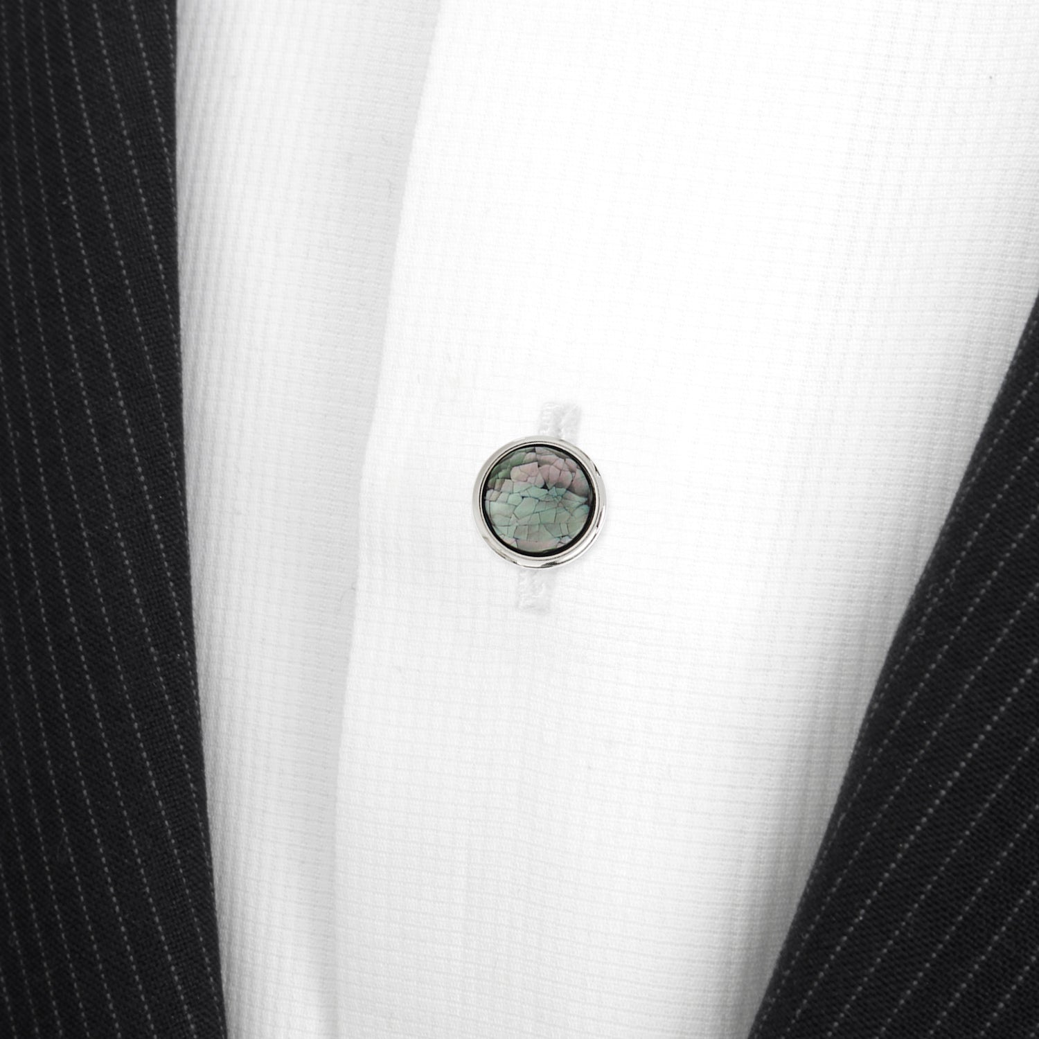 Close-up of a black suit with a white shirt and a round, multicolored gemstone button.