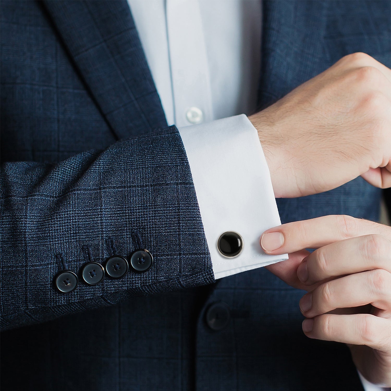 Close-up of a person adjusting the cuff of a dark suit jacket with a white shirt.