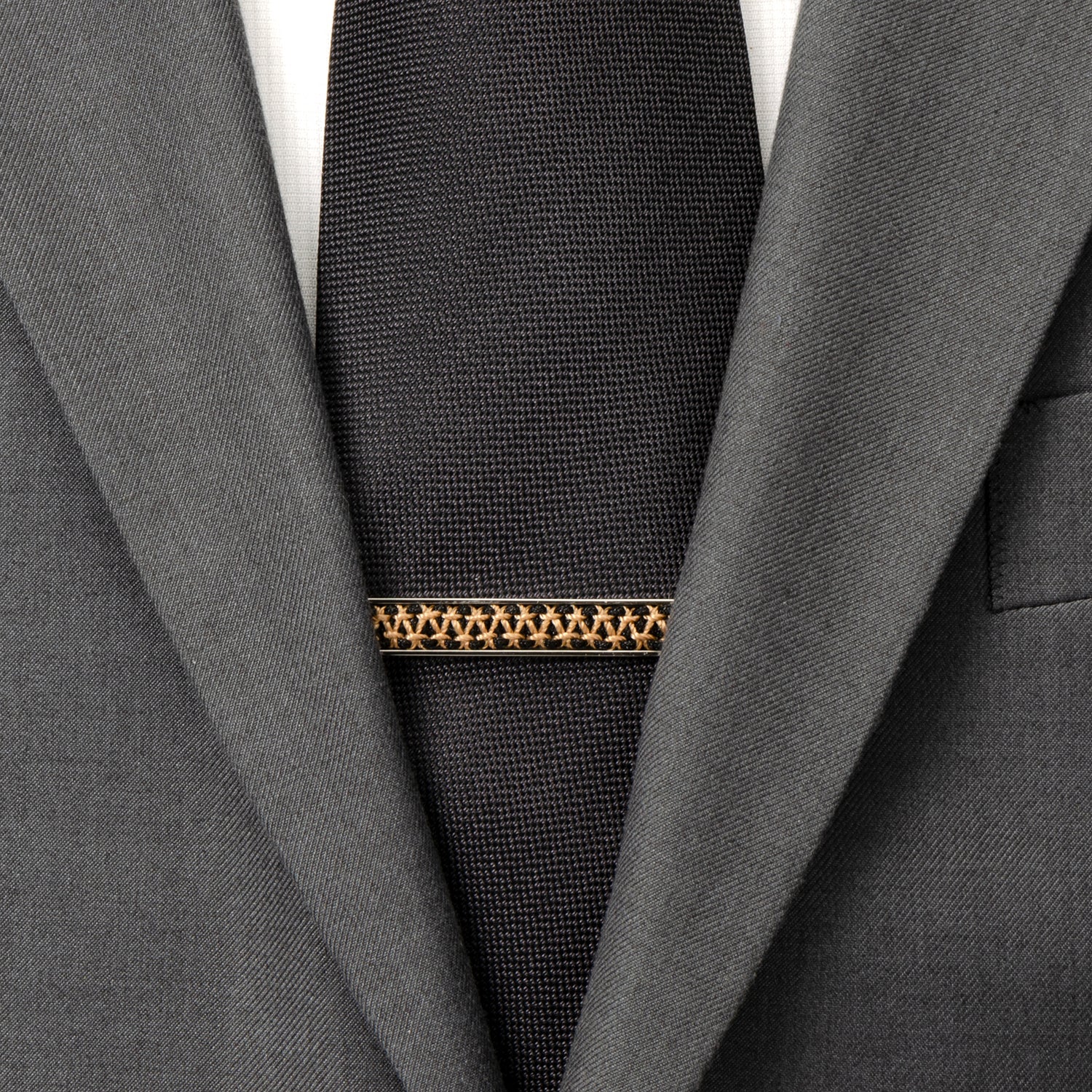 Black tie with a gold and brown patterned tie clip on a gray suit jacket.