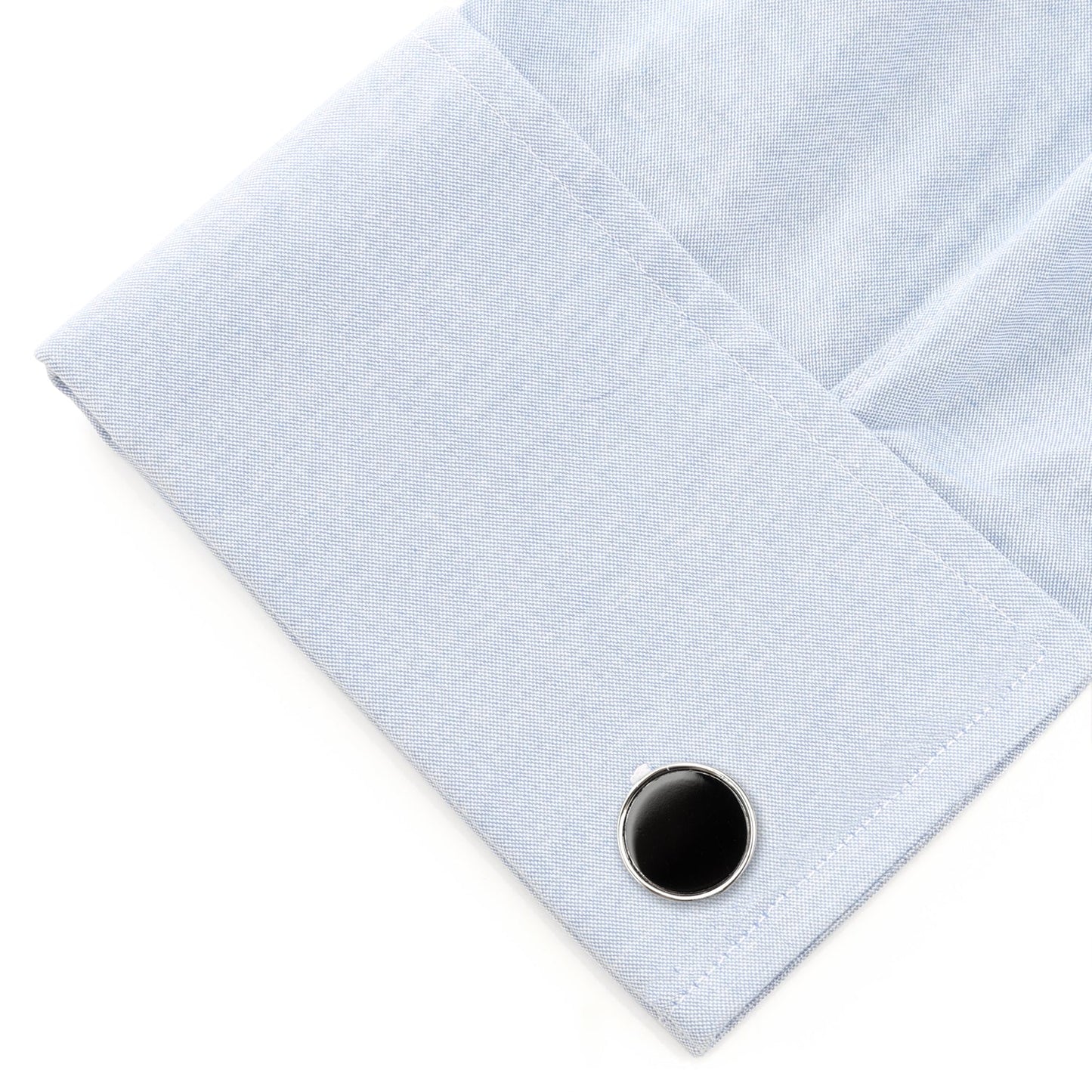 Close-up of a light blue shirt cuff with a black button on a white background