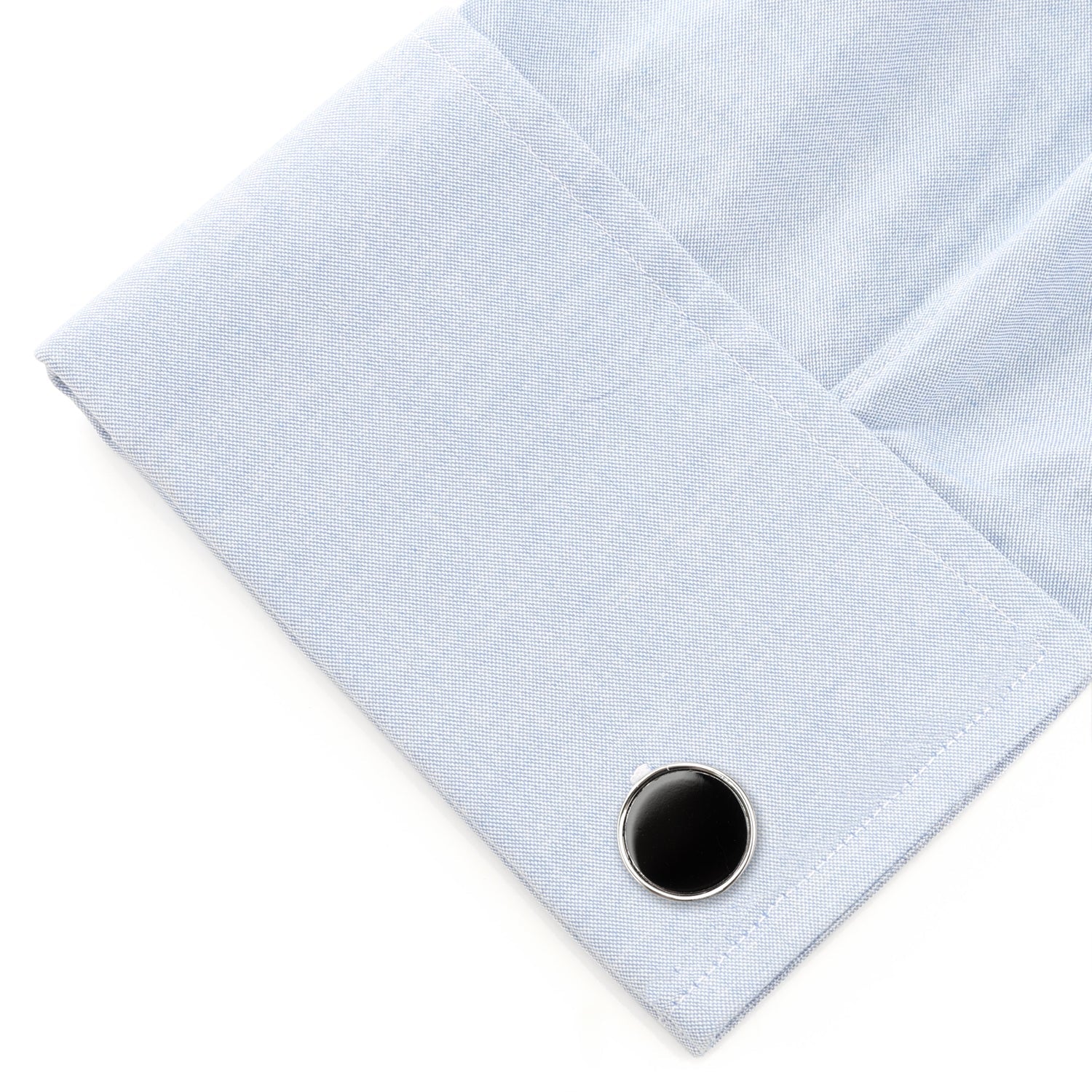 Close-up of a light blue shirt cuff with a black button on a white background