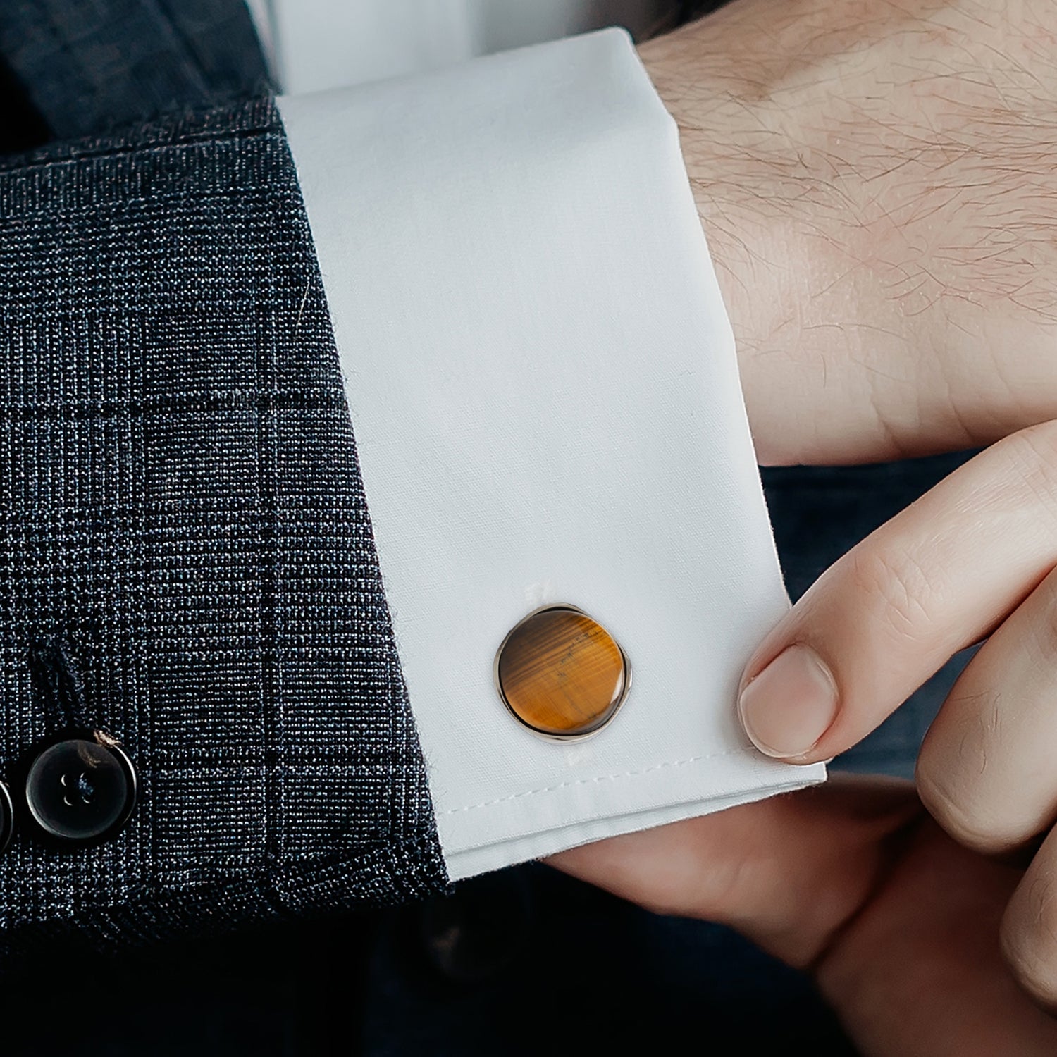 Close-up of a person wearing a dark gray textured jacket with a white shirt cuff and brown tortoiseshell cufflinks.