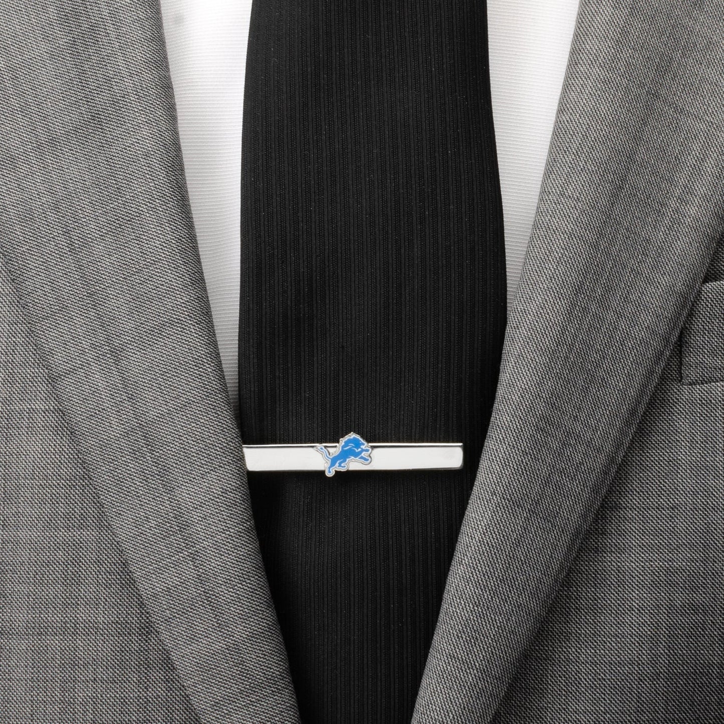 Tie clip with a logo on a black tie against a gray suit jacket.