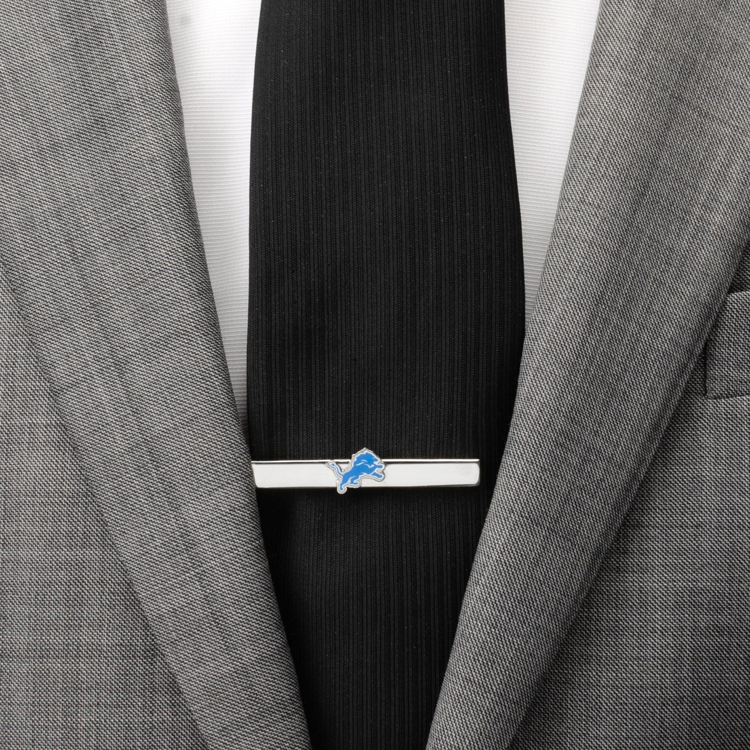 Tie clip with a logo on a black tie against a gray suit jacket.