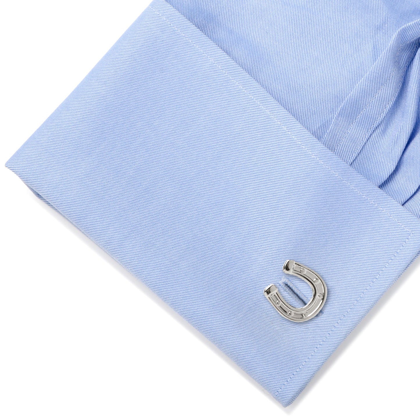 Horseshoe-shaped cufflink on a light blue shirt sleeve