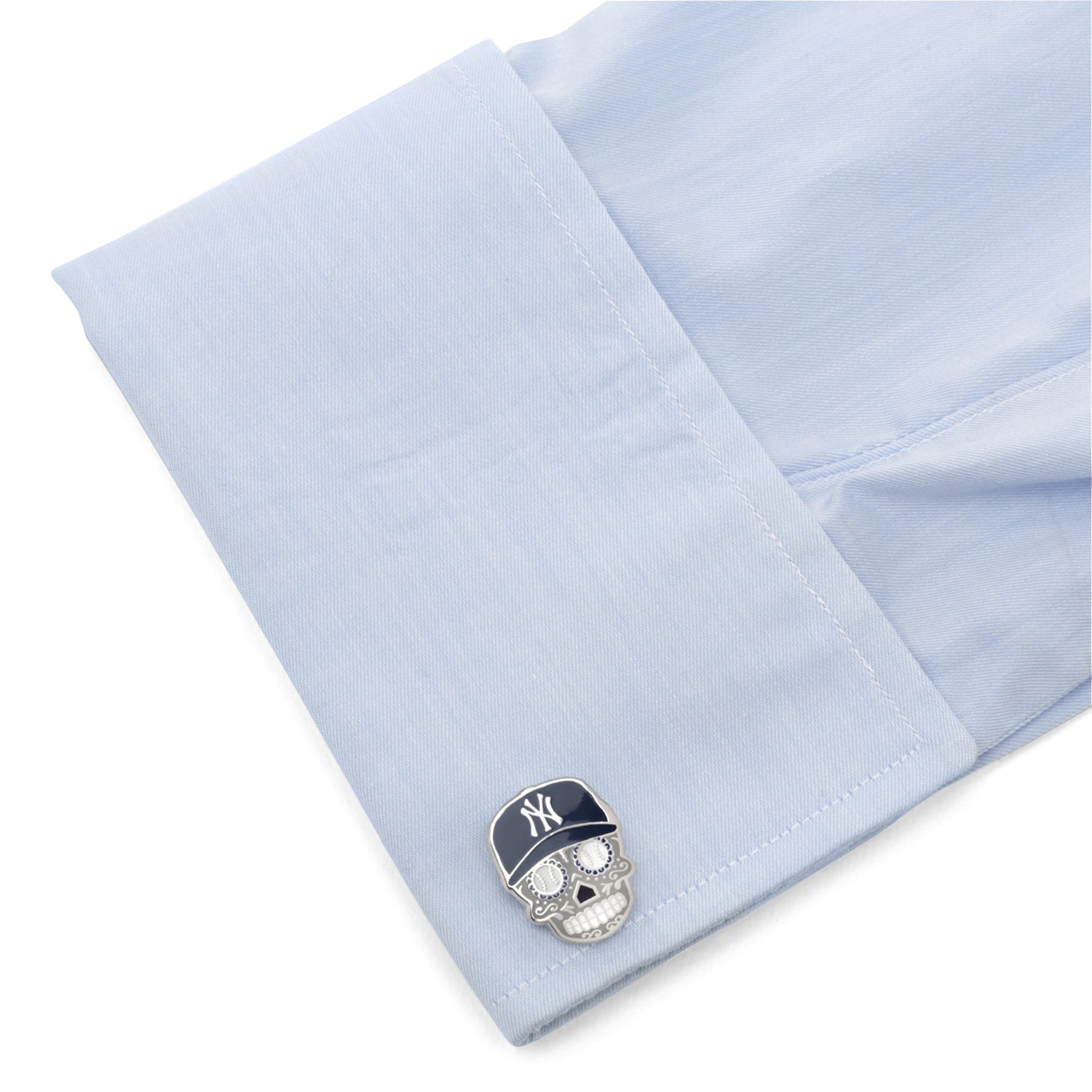 Cufflink with a skull design and cap on light blue shirt cuff