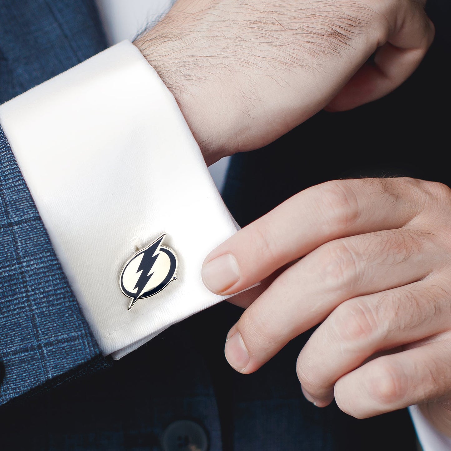 Cufflink with a lightning bolt design on a white cuff against a dark suit background