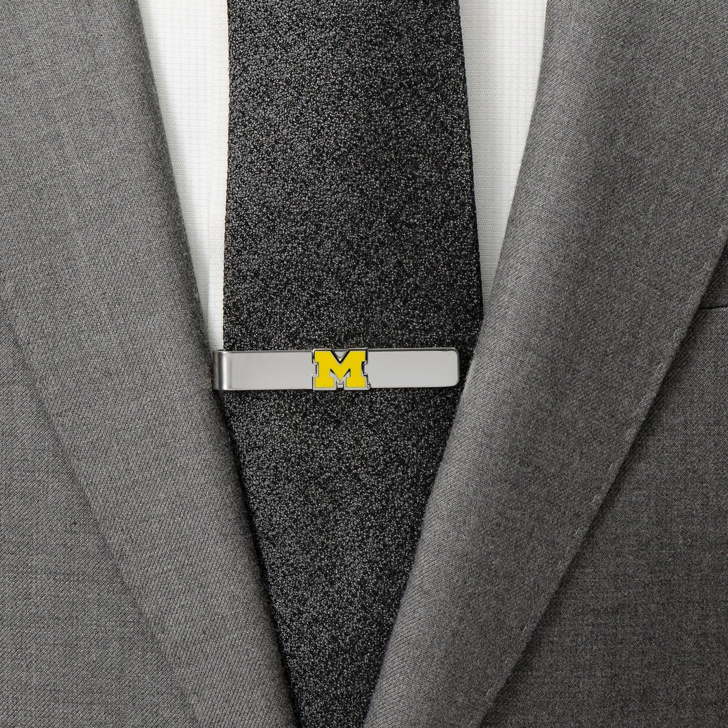 Gray suit jacket with a black tie featuring a yellow 'M' emblem.