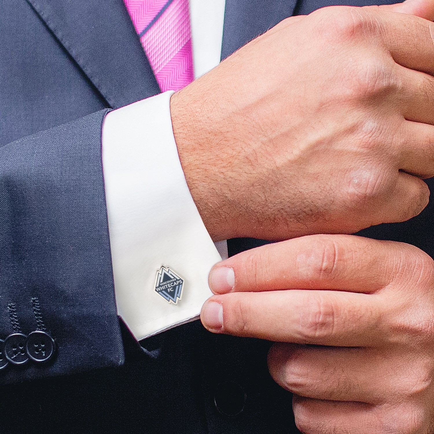 Close-up of a person wearing a suit with a cufflink on a white shirt.