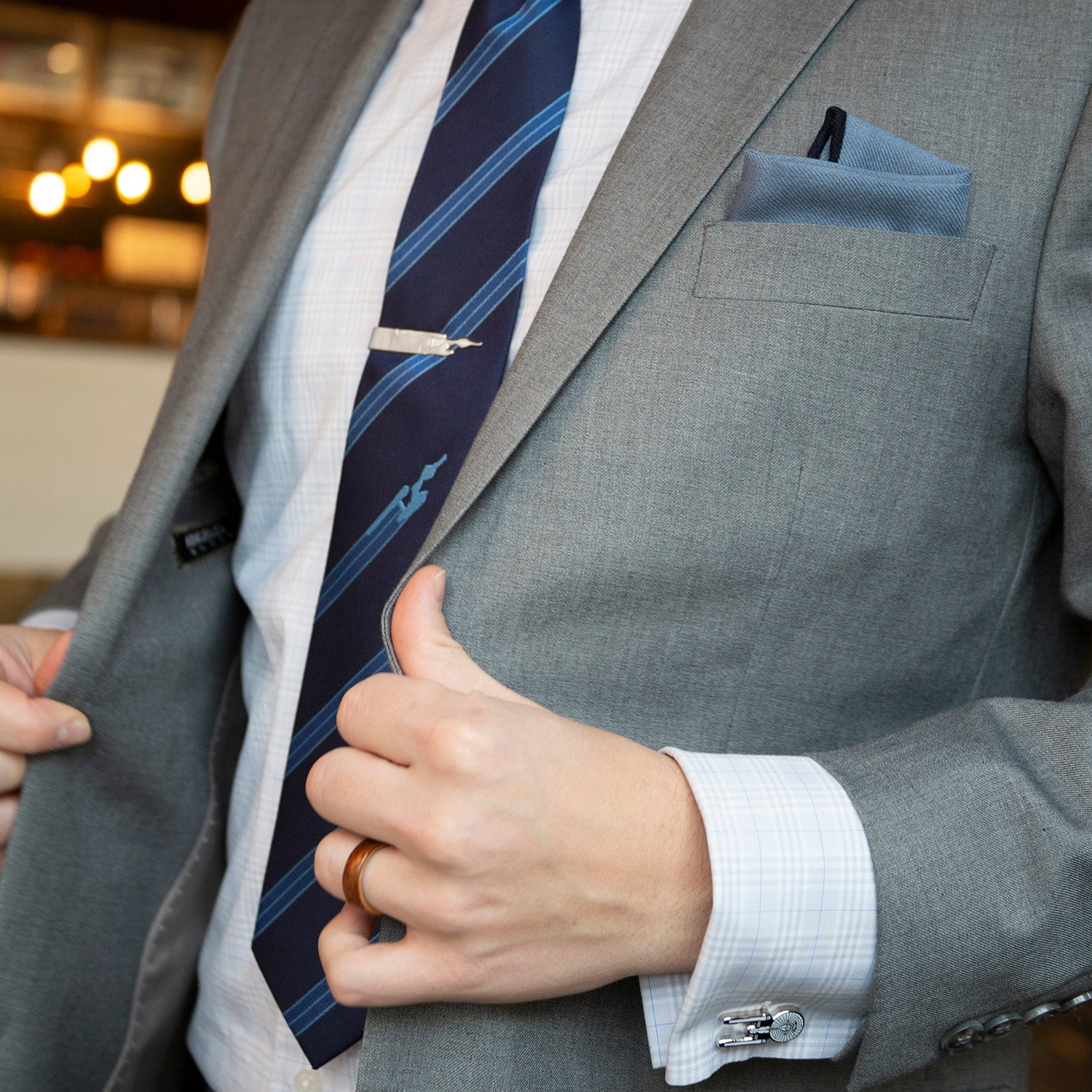 Gray suit jacket with a blue striped tie and pocket square, blurred indoor background