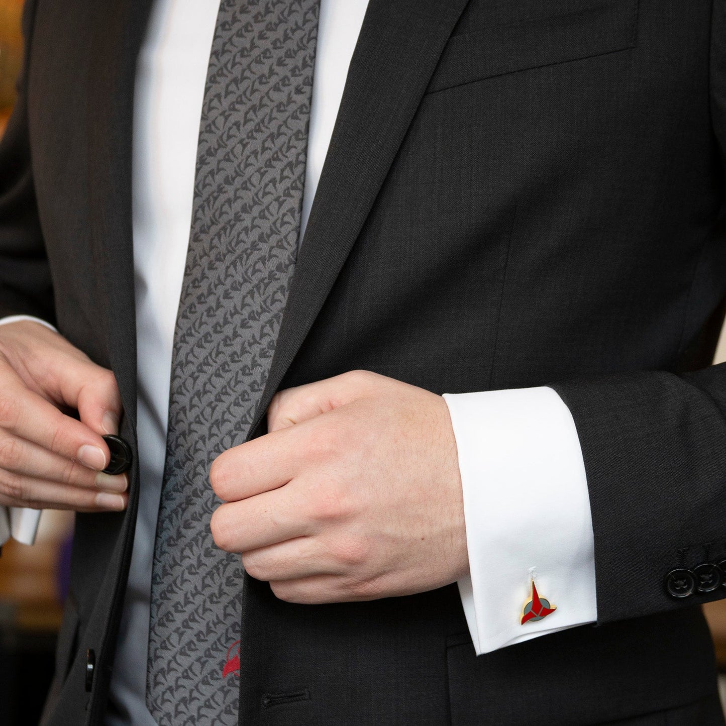 Close-up of a person adjusting a gray patterned tie with a black suit and white shirt.