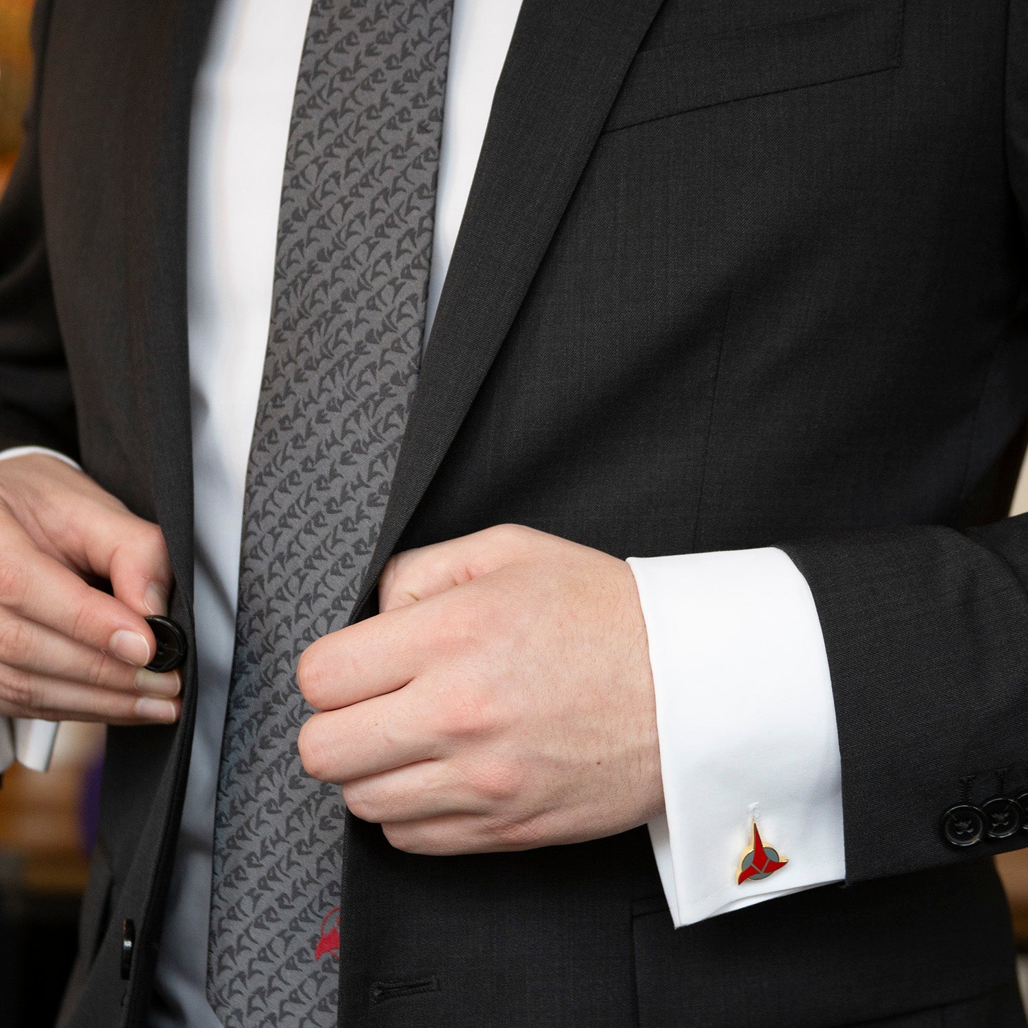Close-up of a person adjusting a gray patterned tie with a black suit and white shirt.