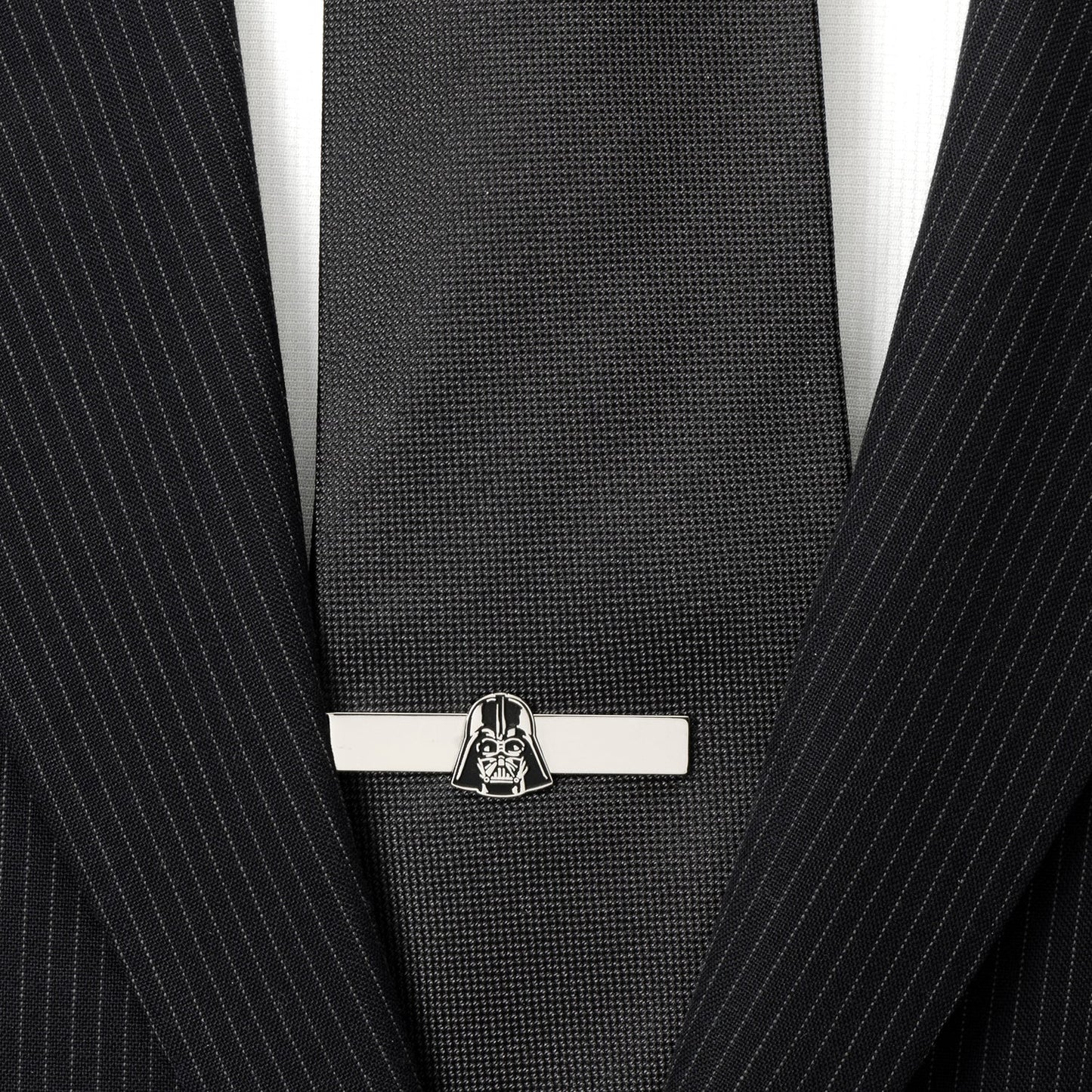 Black tie with a silver tie clip featuring a character design, worn with a black pinstripe suit.
