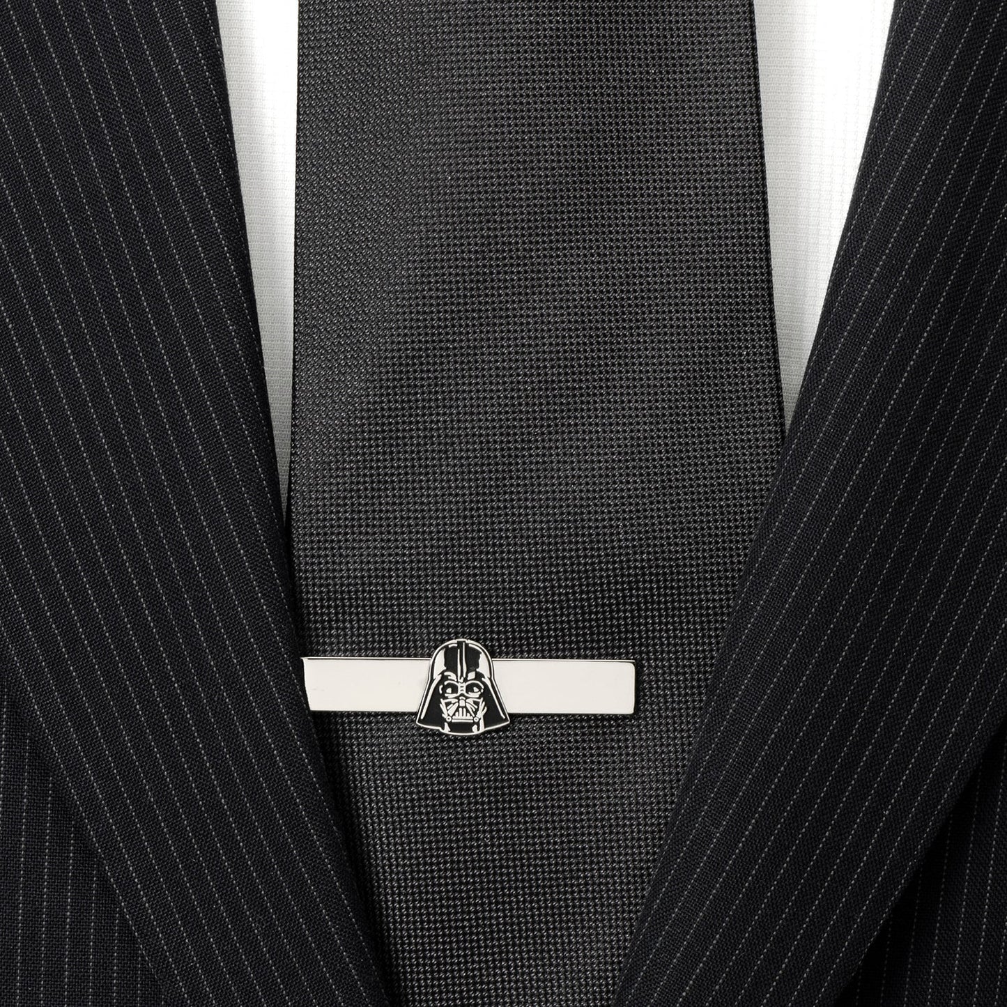 Black tie with a silver tie clip featuring a character design, worn with a black pinstripe suit.