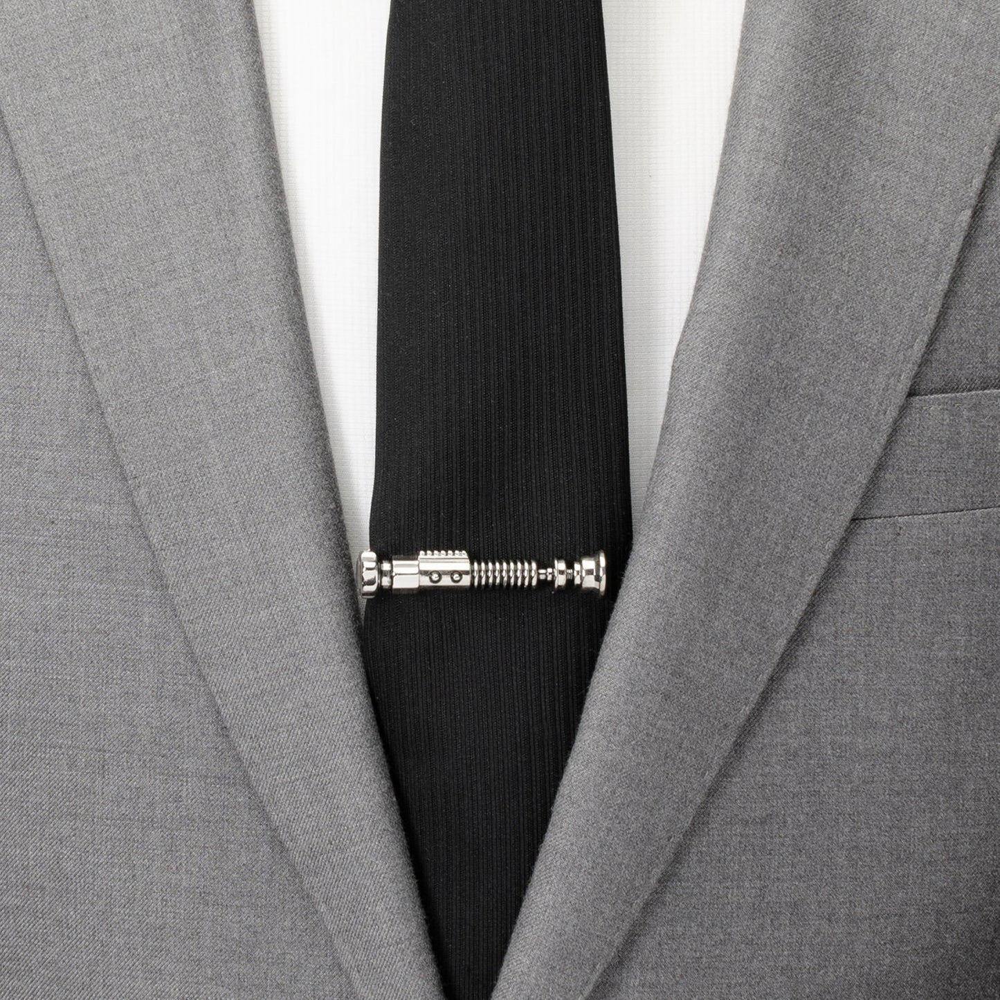 Black tie with a unique design held in place by a silver tie clip against a gray suit jacket.