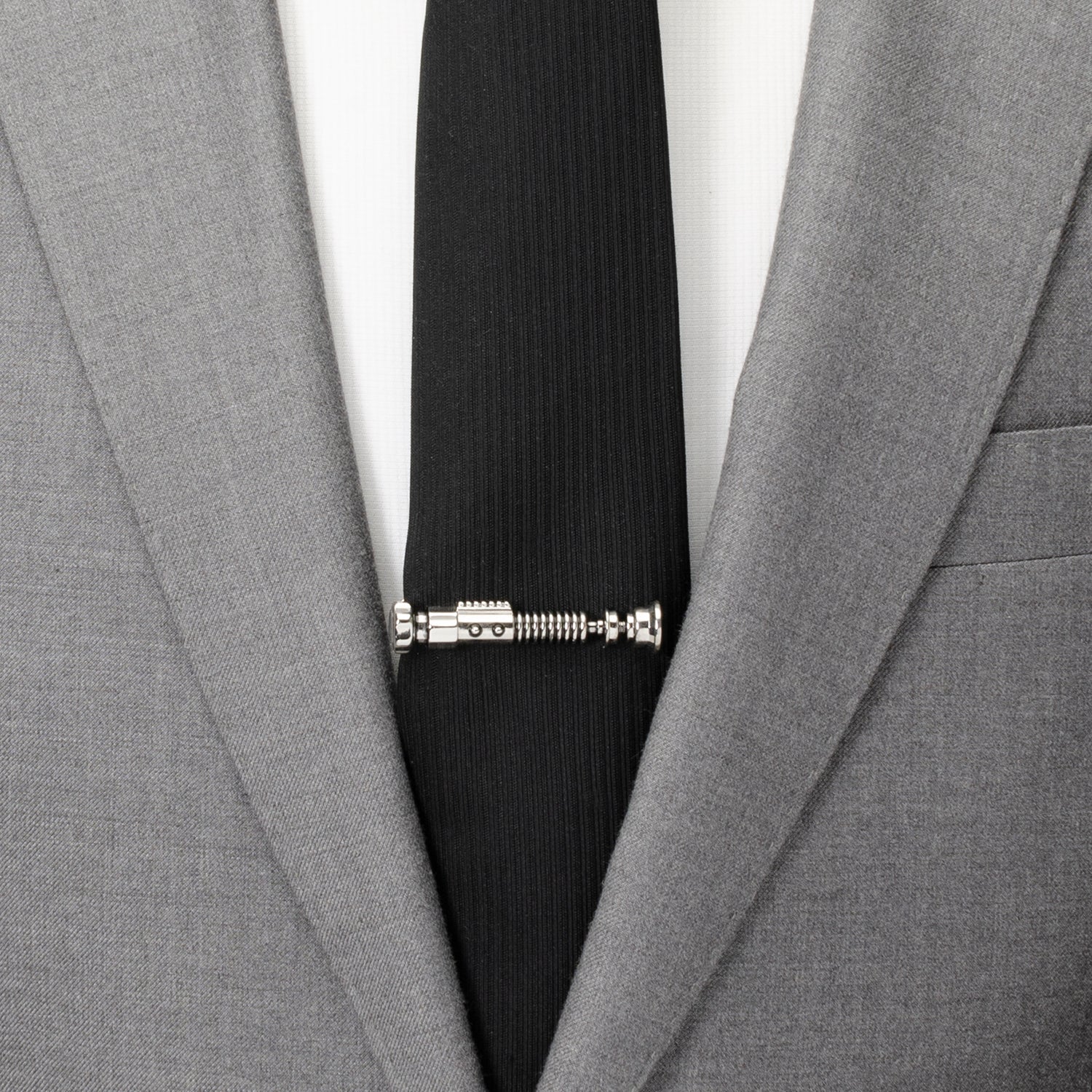 Black tie with a unique design held in place by a silver tie clip against a gray suit jacket.