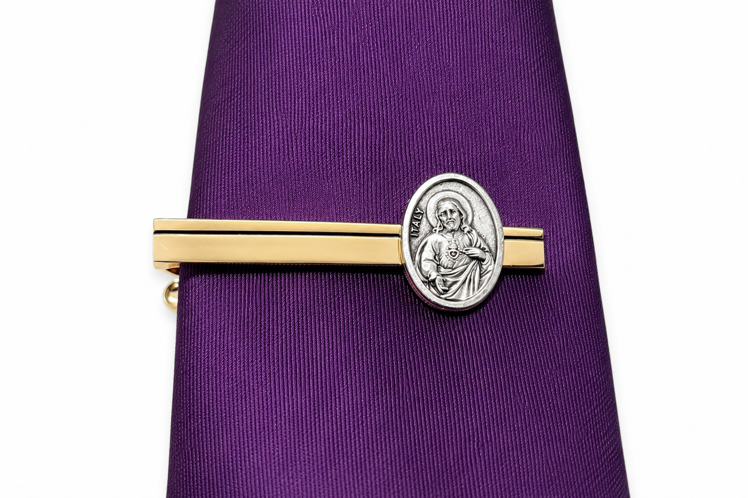 A gold and silver tie bar with an oval Saint Christopher medal, shown on a purple necktie against a white background.