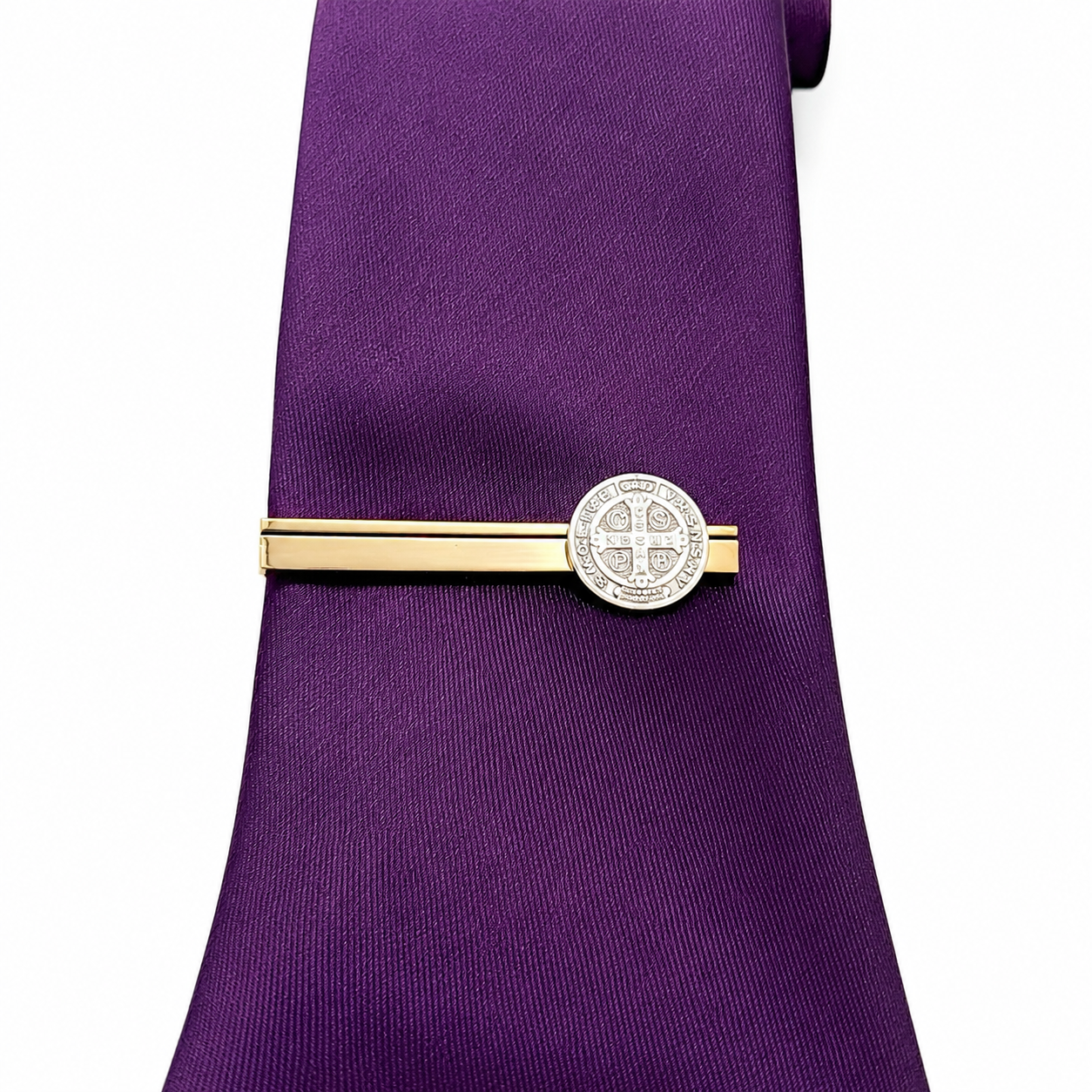 A purple silk necktie with a gold and silver tie clip featuring an engraved cross design, shown against a plain white background.