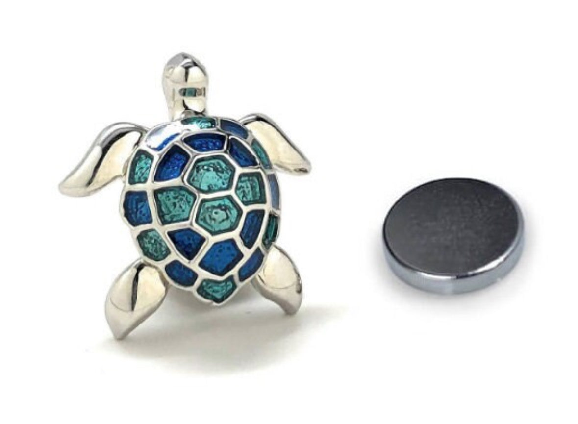 A silver-colored metal pin in the shape of a turtle with a blue and green patterned shell, accompanied by a magnet.