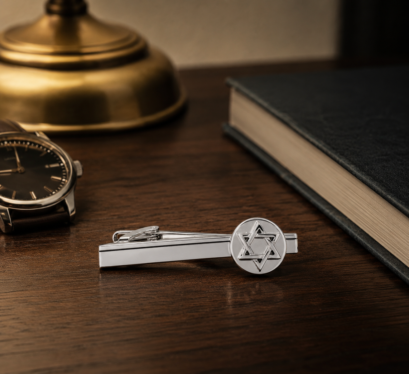 Silver tie clip with Star of David design on a wooden surface with a watch and book in the background.