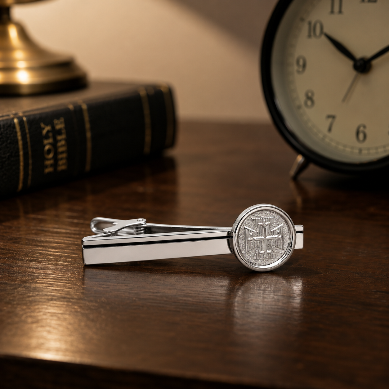 Silver cross tie clip on a wooden surface with a clock and Bible in the background