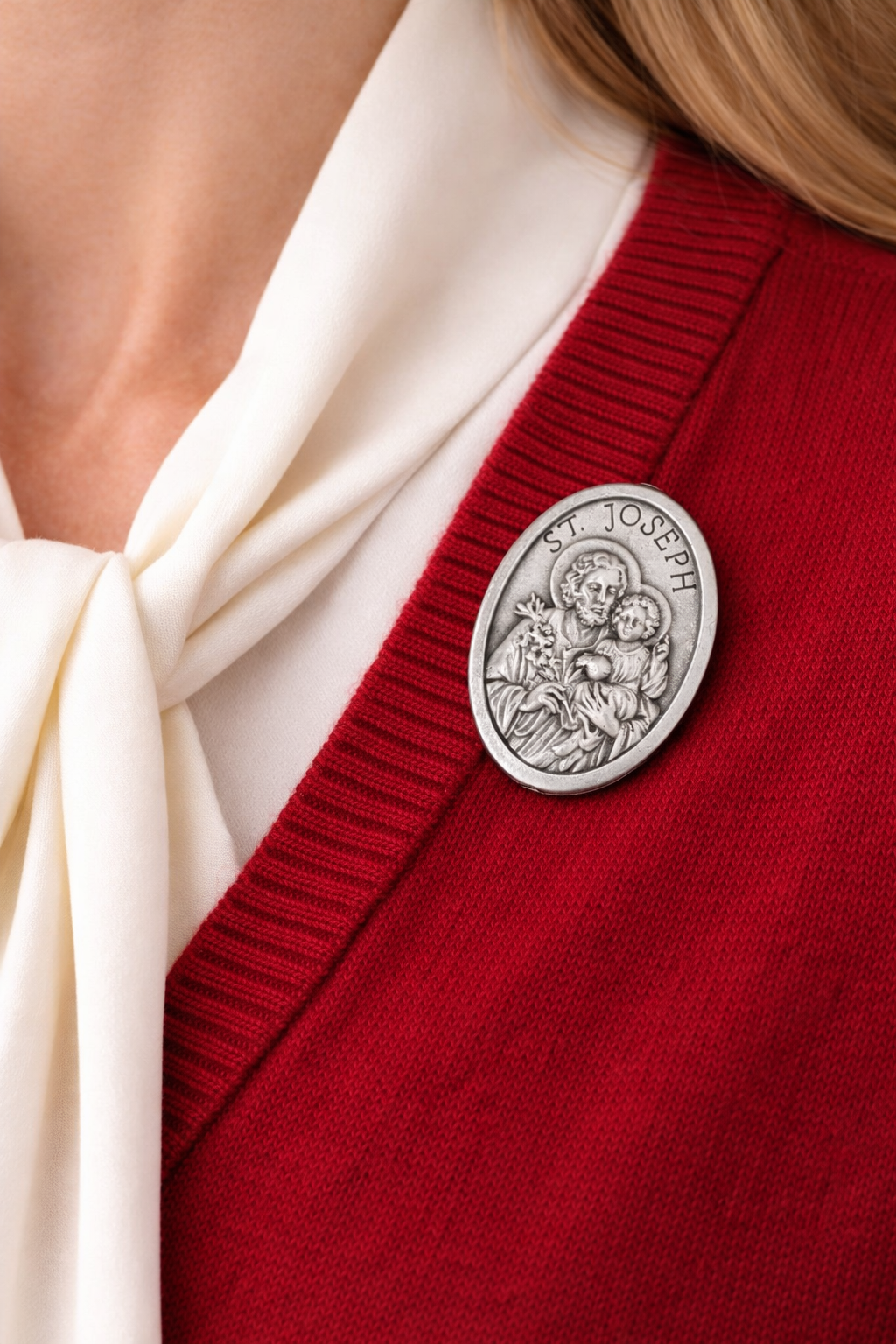 Silver Saint Joseph medallion on a red cardigan with a white scarf