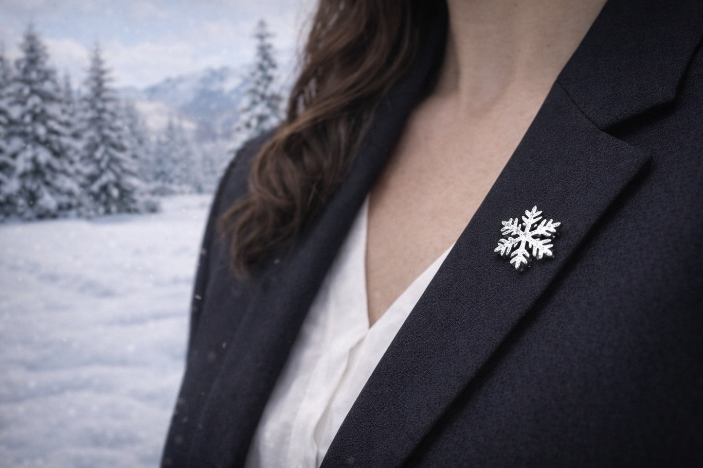 Person wearing a black blazer with a snowflake brooch against a snowy landscape.