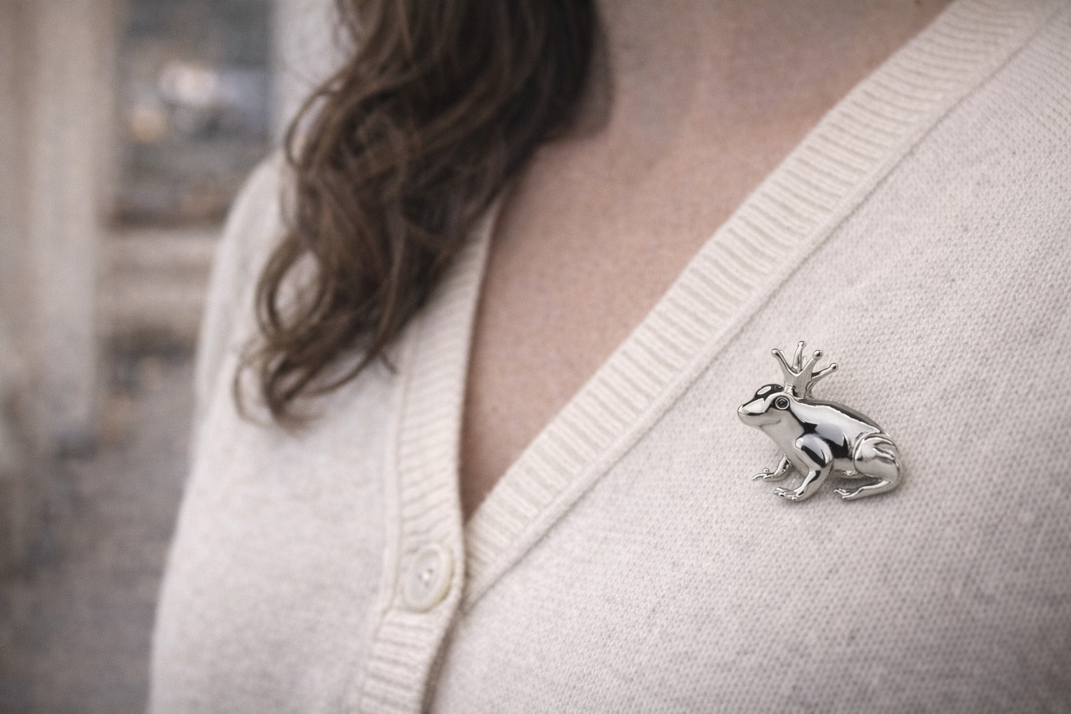 Silver frog brooch on a white sweater