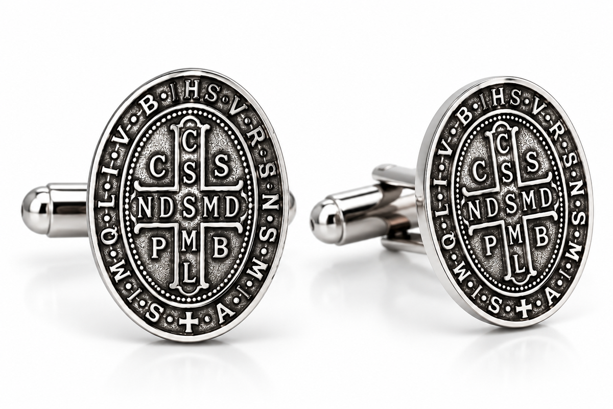 A pair of oval silver-toned cufflinks featuring the Saint Benedict motto 'IN OMNI TRISTE' and the monogram 'CSMD PMB' in an antique finish, displayed on a clean white background.