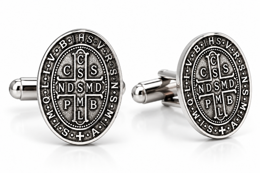 A pair of oval silver-toned cufflinks featuring the Saint Benedict motto 'IN OMNI TRISTE' and the monogram 'CSMD PMB' in an antique finish, displayed on a clean white background.