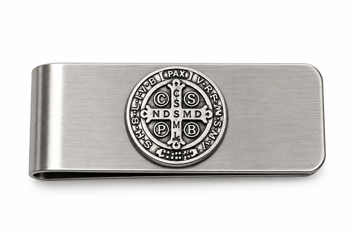A brushed silver metal money clip featuring an embossed circular Saint Benedict monogram in the center, shown on a plain white background.