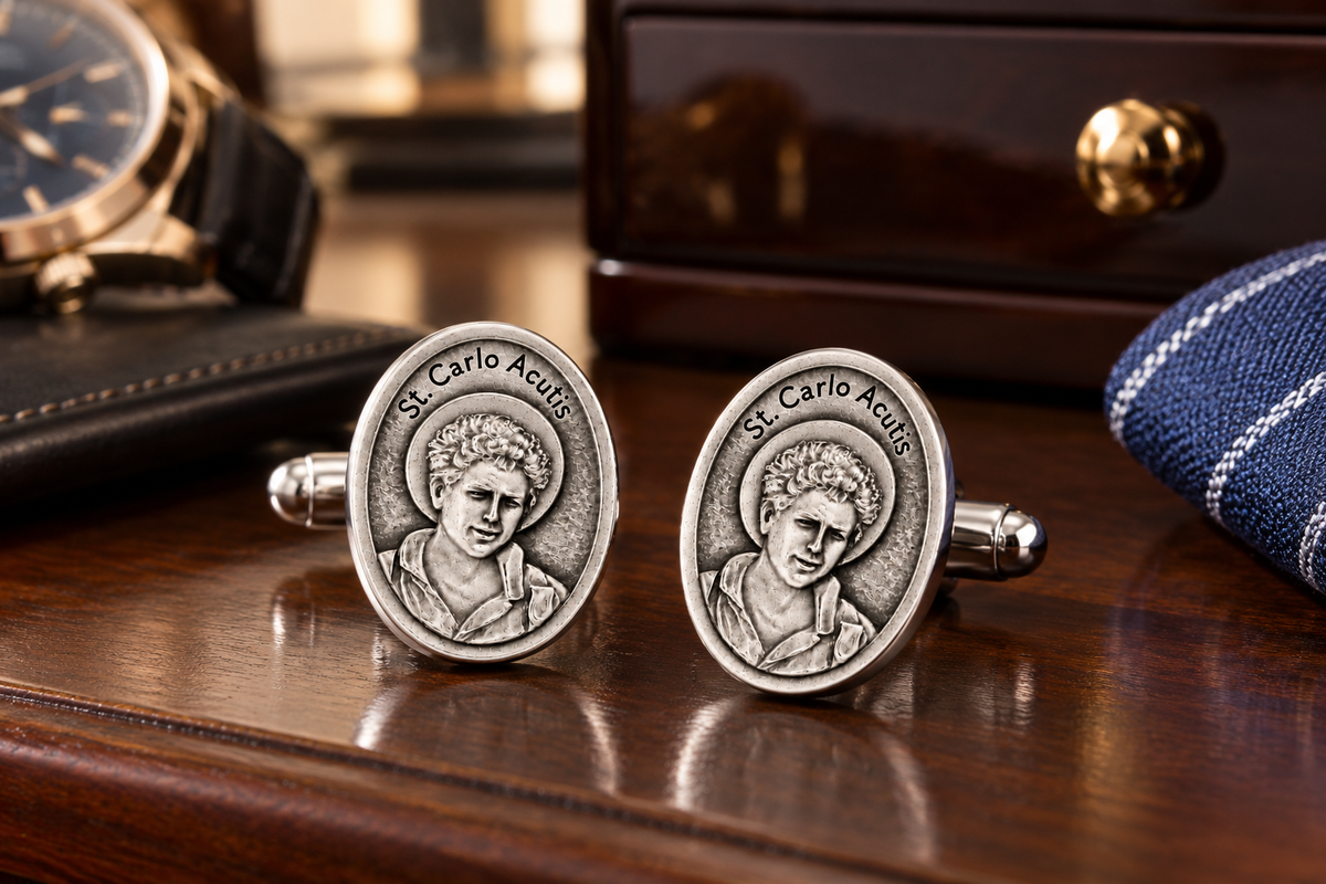 A pair of silver-toned oval cufflinks featuring an engraved portrait of St. Carlo Acuma and the text 'St.