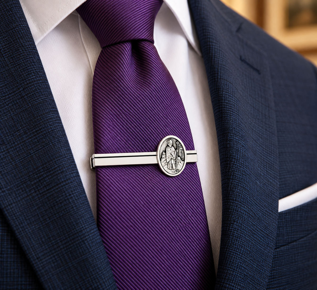A close-up of a purple silk tie with a silver-toned tie bar featuring an oval crest, worn with a white dress shirt and navy blue suit jacket.