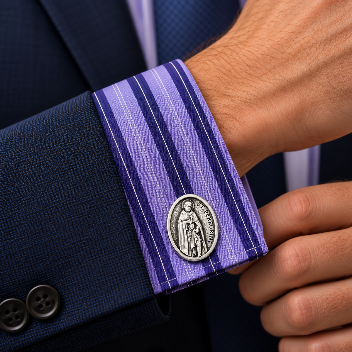 A close-up of a man's wrist wearing a purple and blue striped dress shirt cuff, a navy suit jacket, and a silver-toned Saint Benedict medal cufflink.