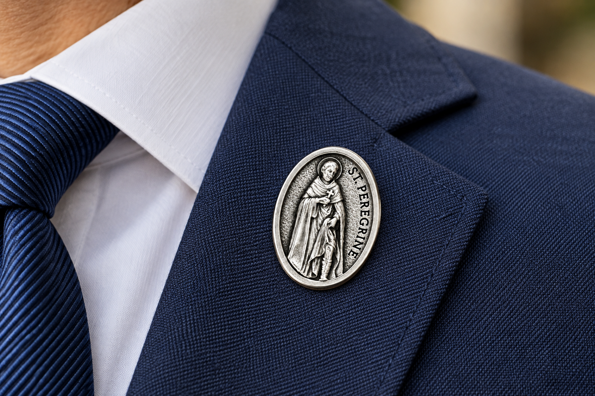 A silver oval Saint Perpetua lapel pin worn on the lapel of a navy blue suit jacket, styled with a white dress shirt and a blue striped tie.