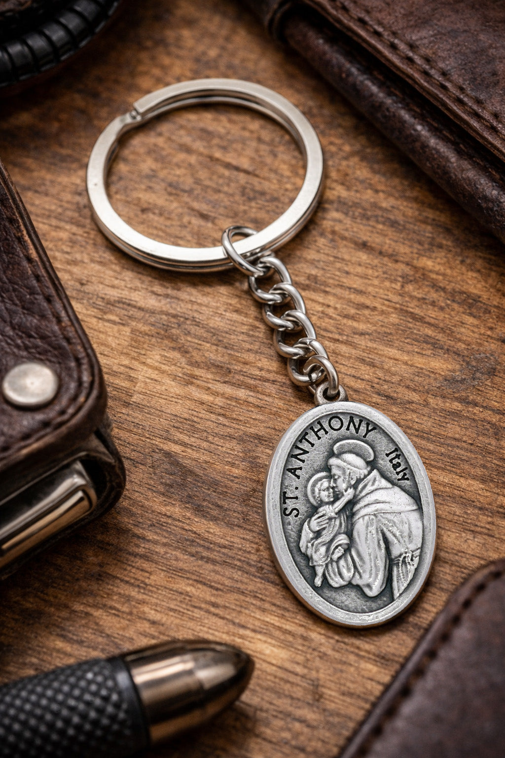 Silver St. Anthony keychain on a wooden surface with a wallet and pen.