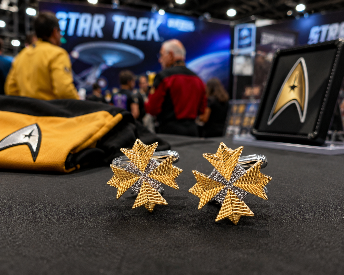 Gold and silver cufflinks with Star Trek logo on a black surface with event background