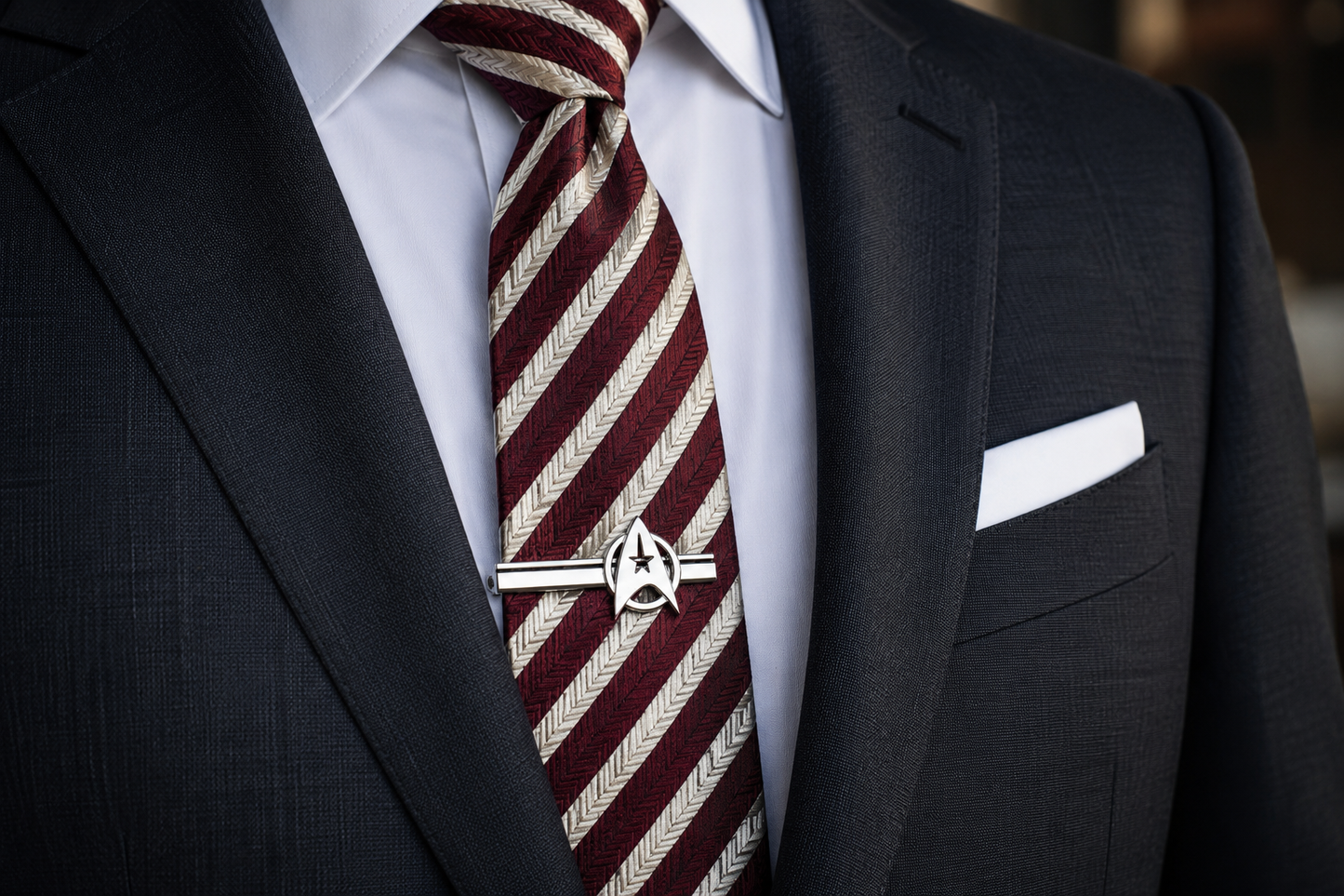 Man wearing a dark suit with a red and white striped tie and a silver tie clip.