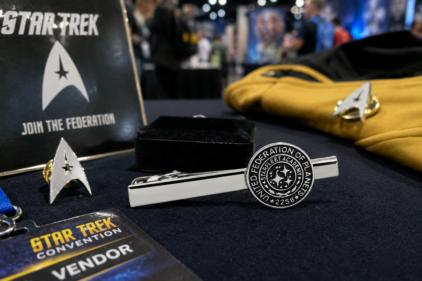 Star Trek-themed merchandise including a tie clip and earrings on a table with a convention vendor sign in the background.