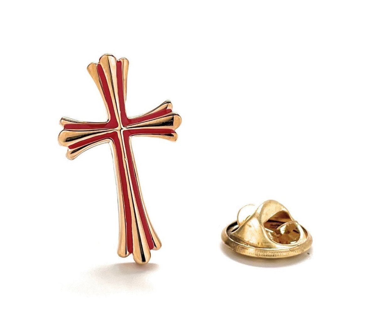 A gold-colored enamel pin in the shape of a cross with red detailing, alongside a gold-colored lapel pin.