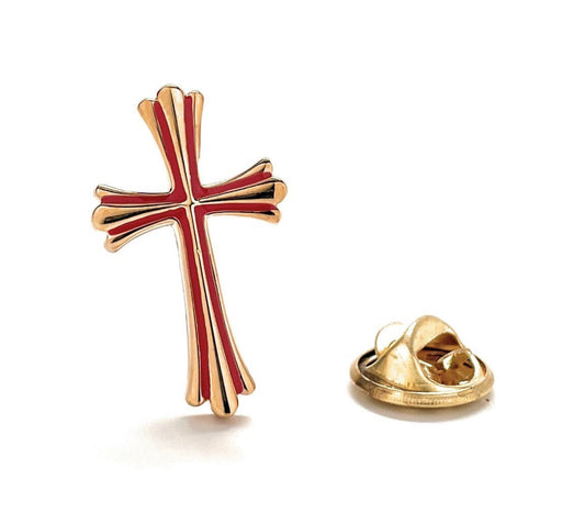 A gold-colored enamel pin in the shape of a cross with red detailing, alongside a gold-colored lapel pin.