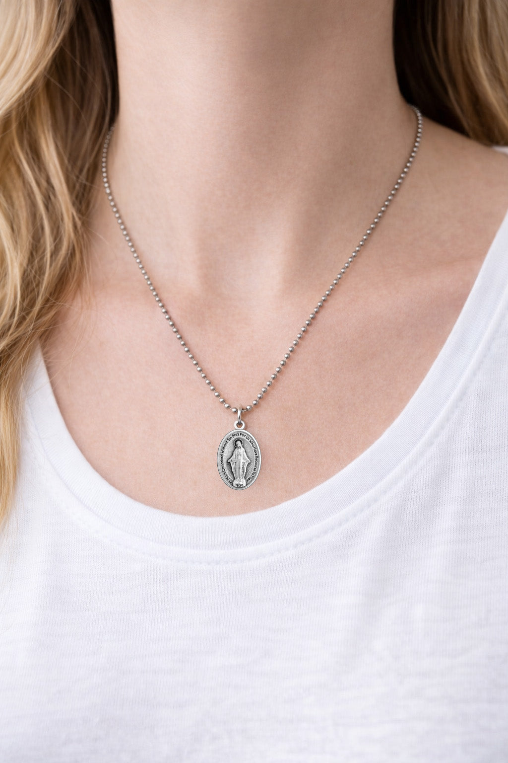 Silver Miraculous Medal necklace with a pendant worn by a person in a white top
