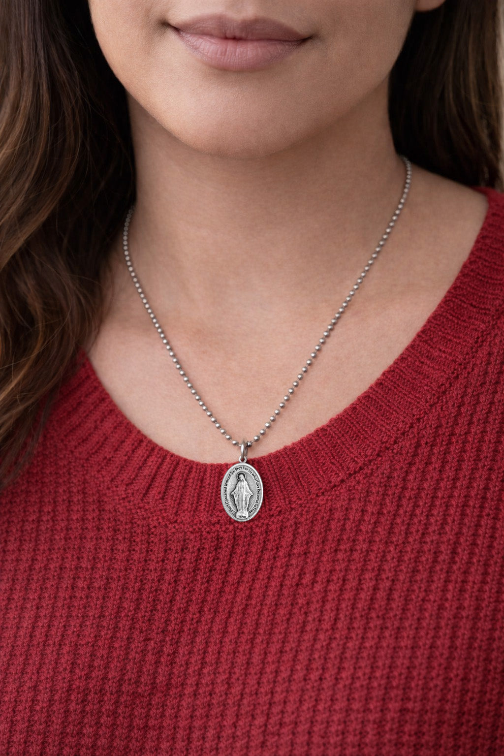 woman wearing a silver Miraculous Medal necklace with a pendant against a red sweater background